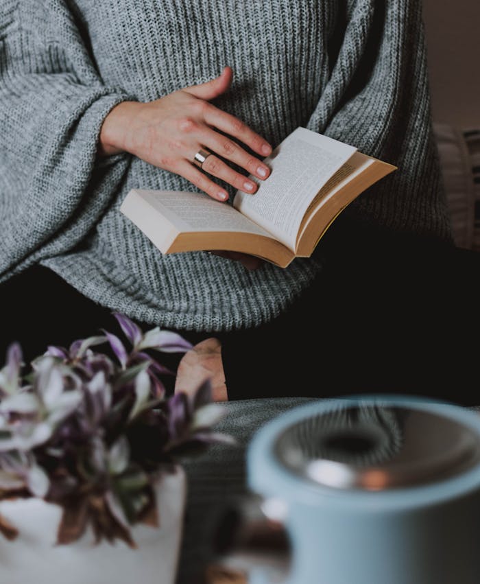 A cozy scene featuring a person reading a book indoors, wearing a warm sweater.